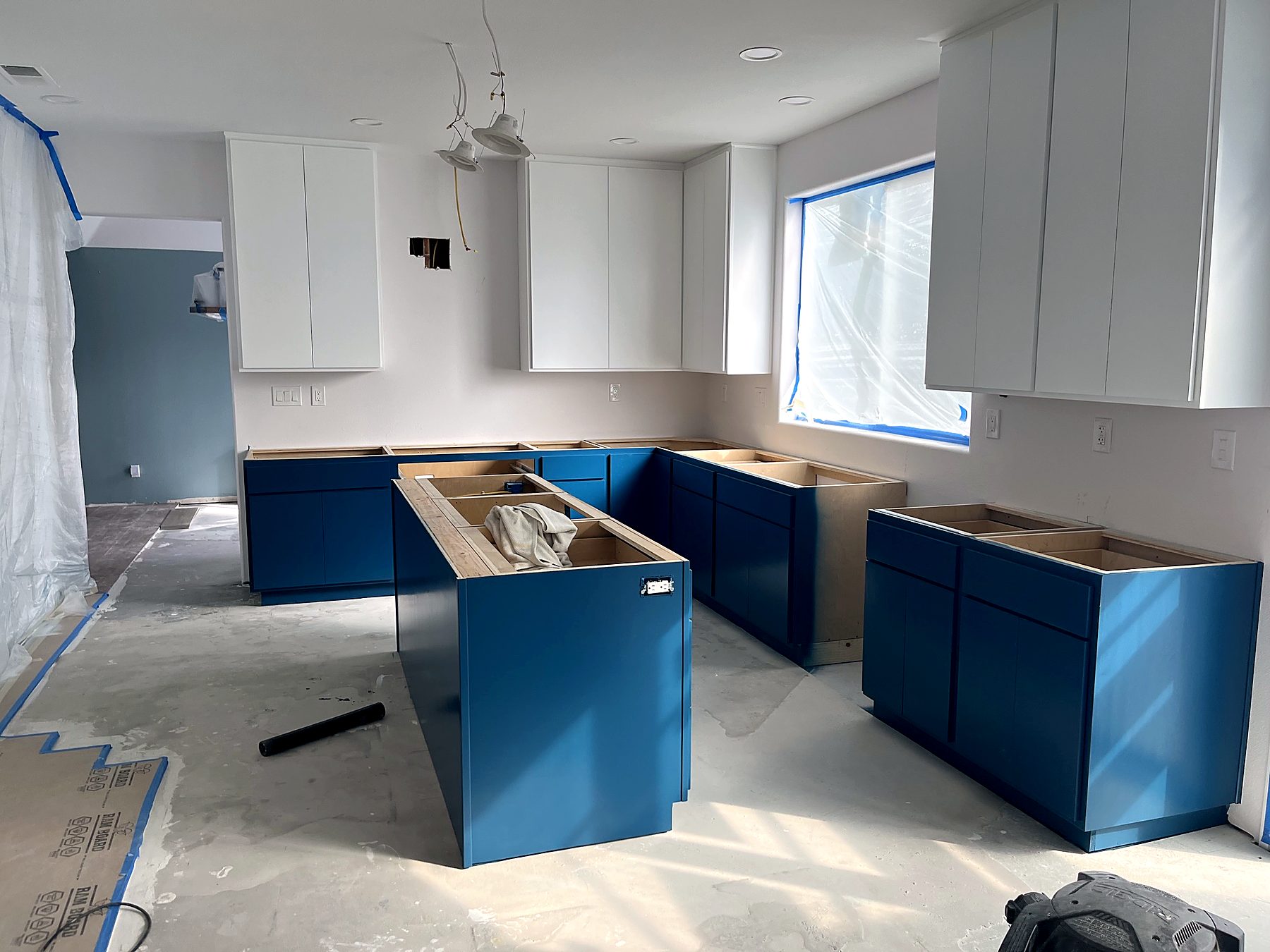 Kitchen remodel in progress with blue base cabinets set on bare subfloor